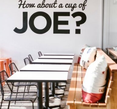Coffee shop with tables, chairs, bench seating with wall graphic saying how about a cup of Joe?
